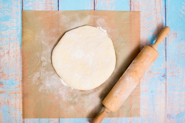 wooden rolling pin over the flat dough over the parchment paper on wooden table - Постная галета с мандаринами