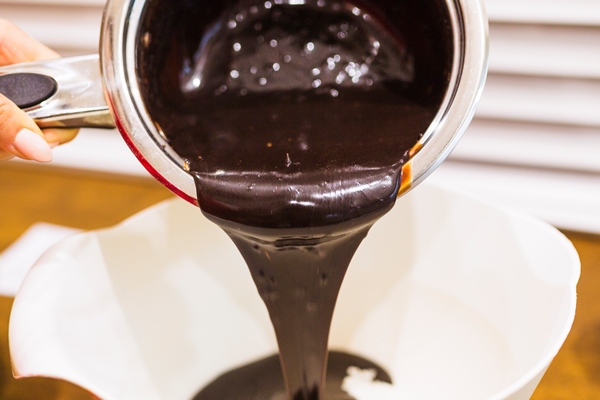 crop hand pouring chocolate sauce into bowl - Шоколадная колбаса с фундуком и печеньем