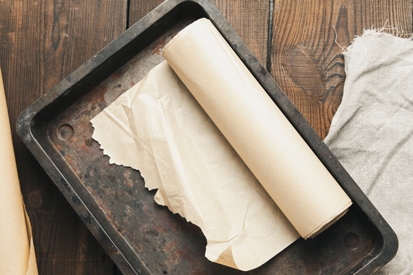 empty rectangular metal pan covered with brown parchment paper and paper rolls on a wooden table top view - Яблочная пастила