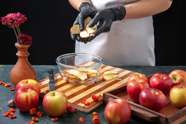 front view female cook putting apples into plate on dark fruit juice diet salad food meal exotic work pie cake - Розочки из слоёного теста с яблоками