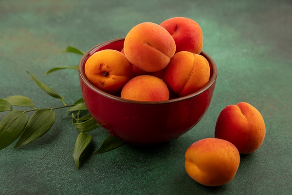 side view of apricots in bowl with leaves on green background - Как правильно варить и хранить варенье