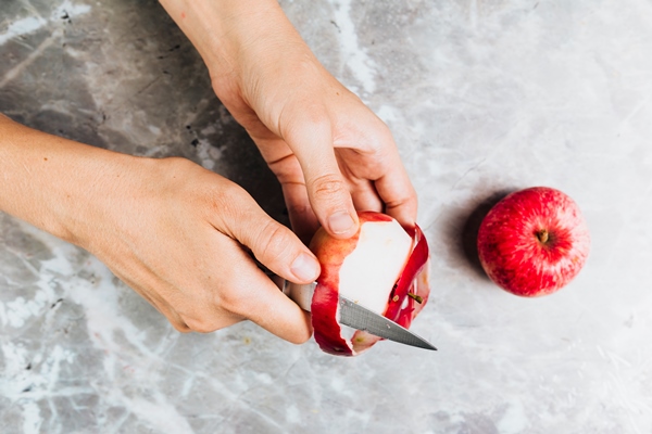 top view of hands peeling an apple on marble background - Яблочно-свекольная окрошка