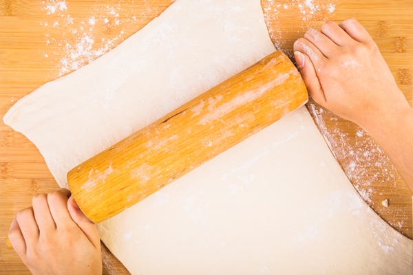 woman s hand rolling dough with rolling pin - Постное слоёное бездрожжевое тесто
