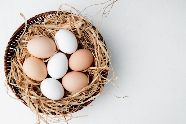 basket full of eggs in nest on white table - Яйцо пашот с авокадо и зерновым хлебцем