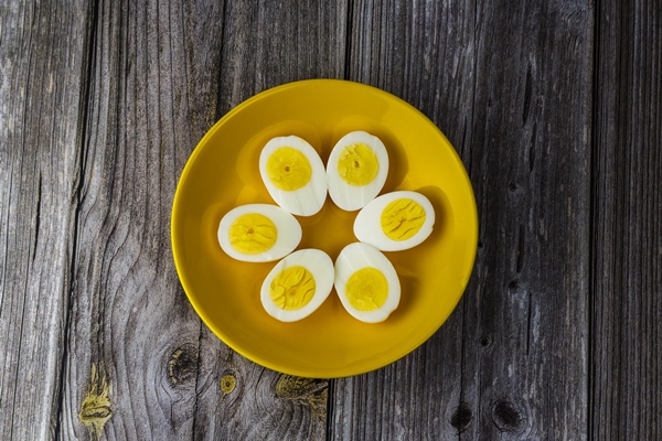 boiled egg halves in a yellow bowl on wooden table - Бутерброд с авокадо и яйцом