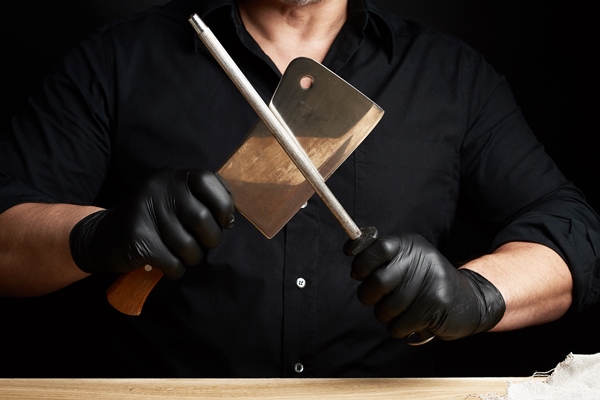 chef in a black shirt and black latex gloves sharpen a kitchen knife onn iron sharpener with a handle - Хозяйке на заметку: виды кухонных ножей