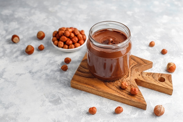 chocolate spread or nougat cream with hazelnuts in glass jar on concrete copyspace - Тосты для детей на завтрак