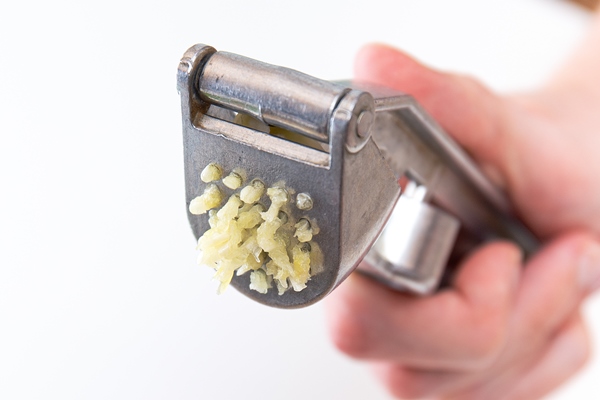 male hands hold a garlic press or garlic squeezer kitchen tool for preparing and preparing salads dishes - Рулет из лаваша с творогом, сыром и зеленью