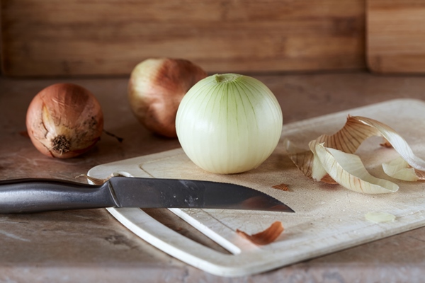 onions and onion peels with knife on cutting board on kitchen table - Овощной салат с редисом и пекинской капустой