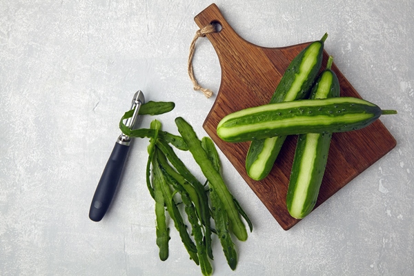 peeled cucumbers on a wooden cutting board with a vegetable peeler and peels - Хозяйке на заметку: виды кухонных ножей