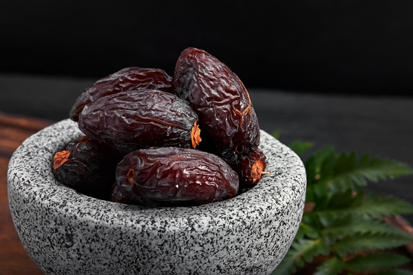 bowl of dried dates on dark wooden surface from side view - Финиковый латте
