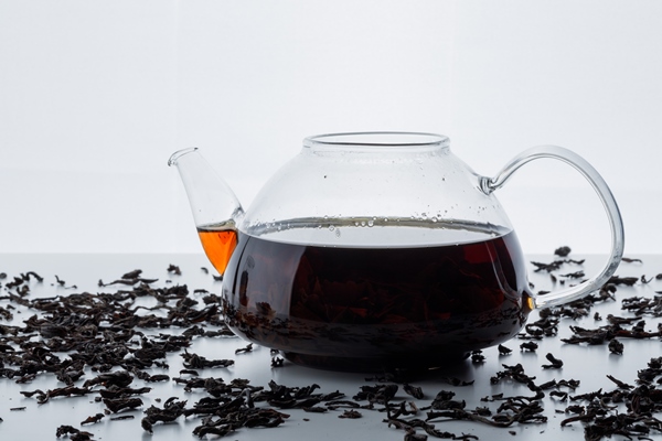 brewed tea in a glass teapot with dry black tea side view on a white surface - Пунш безалкогольный