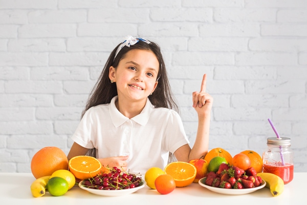 colorful fruits in front of a girl pointing finger upward - Организация правильного питания детей