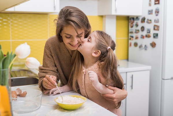 daughter kissing mother while cooking in kitchen - Организация правильного питания детей