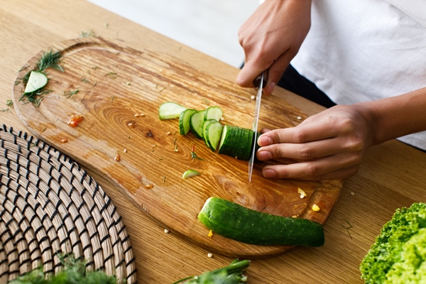 from above woman is cutting a cucumber on a kitchen desk - Салат из свежих помидоров и огурцов (школьное питание)