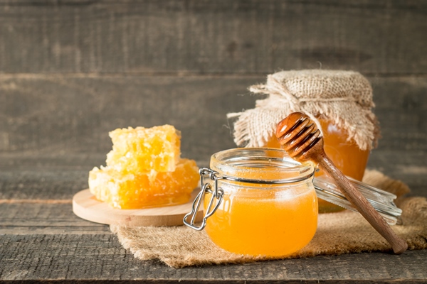 honey dripping from a wooden honey dipper in a jar on wooden grey rustic - Салатная заправка с кунжутом и маком