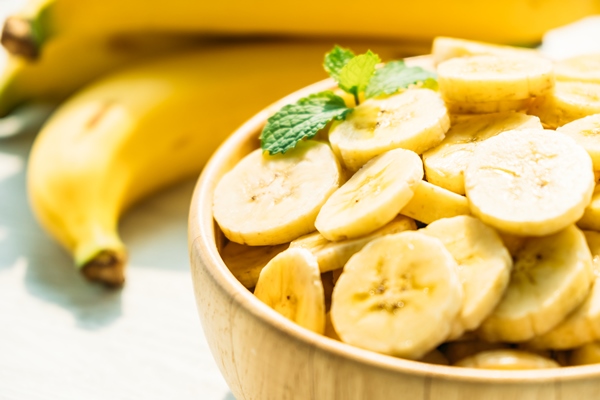 raw yellow banana slices in wooden bowl - Горячий банановый раф
