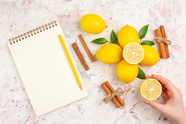 top view fresh lemons cut lemon in female hand cinnamon sticks yellow pencil in female hand on bright isolated surface - Пунш безалкогольный