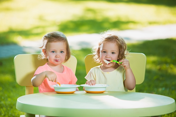 two little girls sitting at a table and eating together against green lawn 1 - Организация правильного питания детей