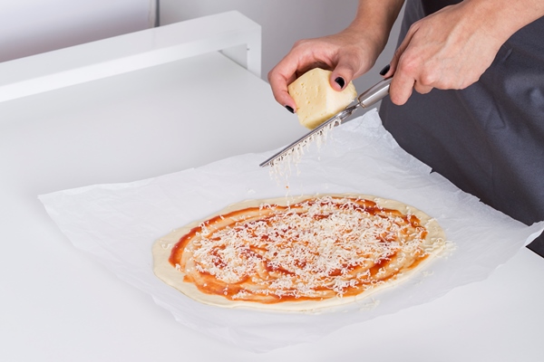 young woman grating the cheese on homemade dough pizza - Быстрая пицца в микроволновке