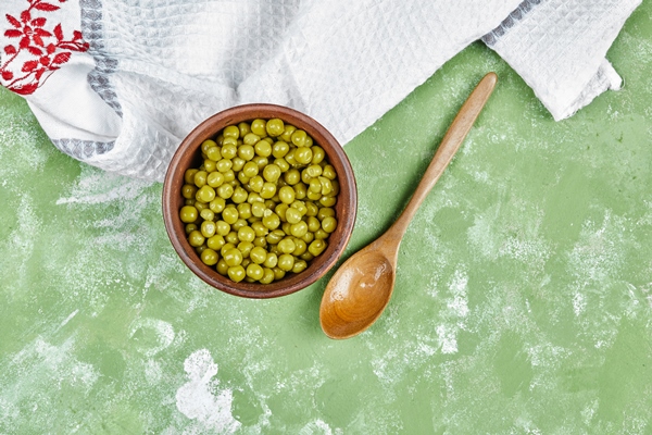 a bowl of boiled green peas with a wooden spoon and a tablecloth - Зелёный горошек (школьное питание)