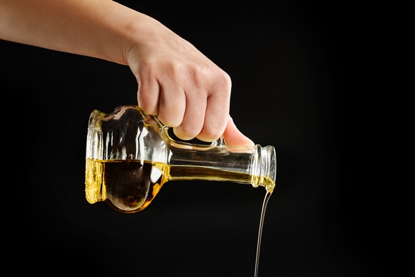 a female hand pours freshly prepared salad from a glass bottle with olive oil - Салат из белокочанной капусты с морковью и сахаром (школьное питание)