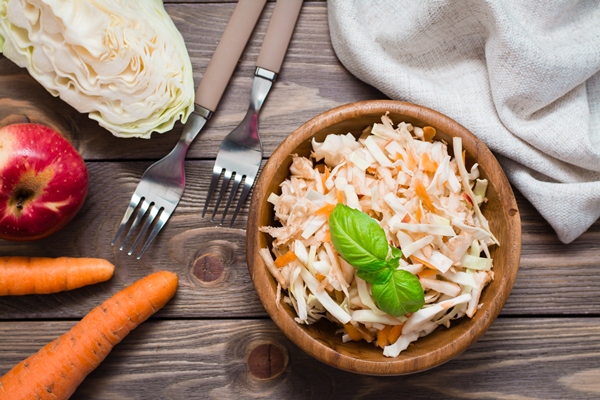 american ready to eat cole slaw salad made from cabbage celery carrots and apples with basil leaves in a wooden plate and ingredients for cooking on a wooden table healthy and eating concept - Салат из белокочанной капусты с морковью и яблоками (школьное питание)