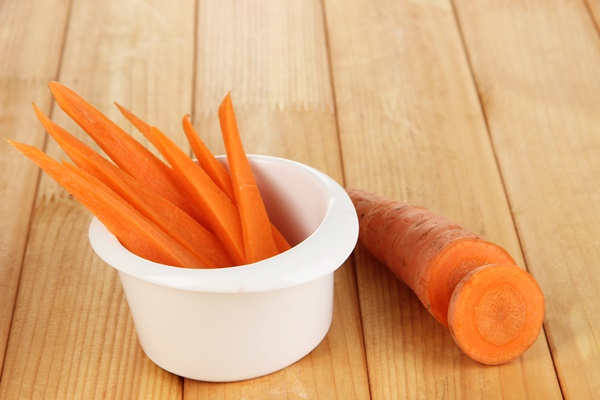 bright fresh carrot cut up slices in bowl on wooden table closeup - Морковь отварная дольками (школьное питание)