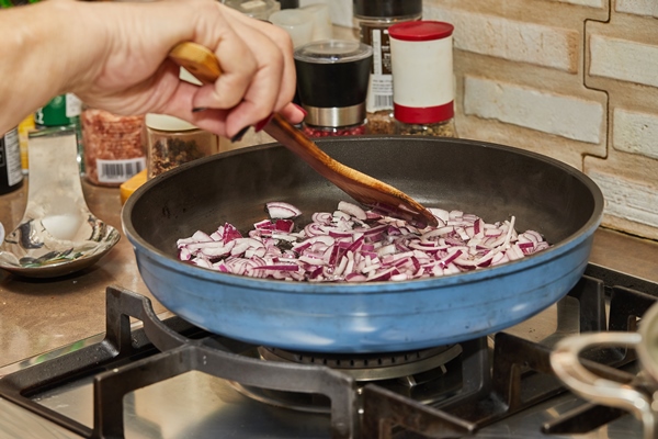 chef stirs purple onions into frying pan on gas stove - Тушёная свёкла со сметаной и ламинарией (школьное питание)