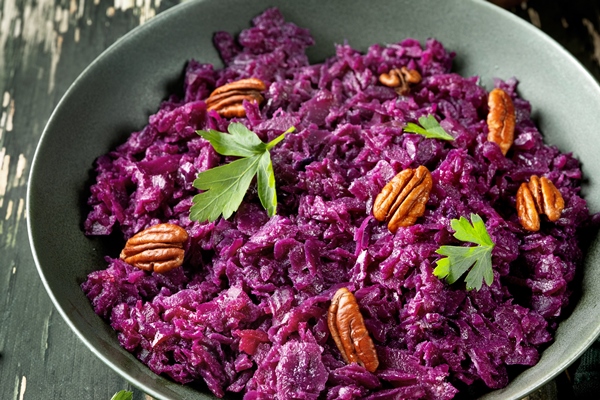 close up of a plate with colorful red cabbage salad and apples on green background - Салат из свёклы с курагой и изюмом (школьное питание)
