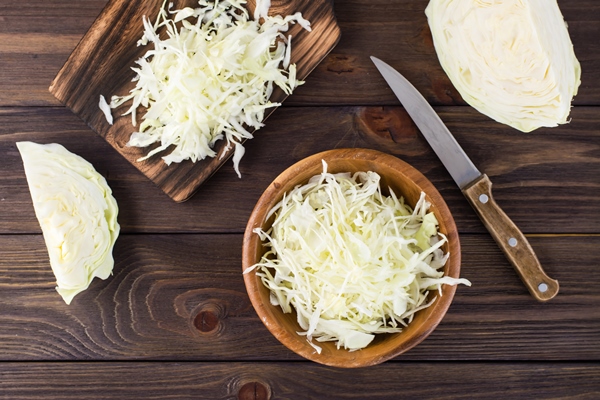 fresh raw cabbage cut into strips in a bowl and pieces of cabbage on a wooden table vegetarian diet top view - Салат из белокочанной капусты с морковью и сахаром (школьное питание)