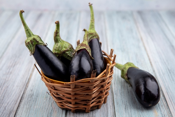 side view of eggplants in basket and on wooden background - Овощная икра (школьное питание)