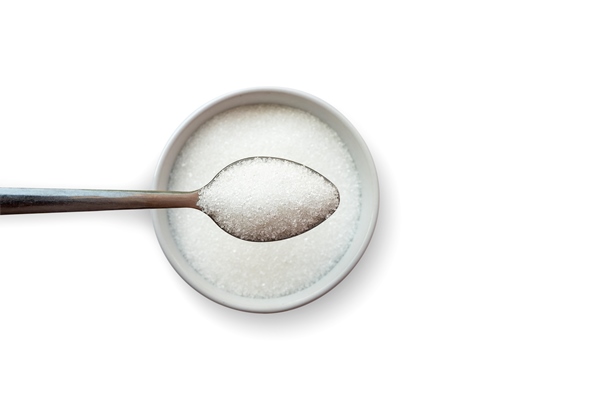 top view of the sugar in teaspoons that are on a separate sugar cup on a white background concept of reducing the amount of sugar in food and drinks - Тушёная морковь с изюмом и ламинарией (школьное питание)