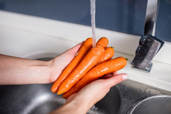 woman washing carrots at kitchen washbasin - Салат из белокочанной капусты с морковью и сахаром (школьное питание)
