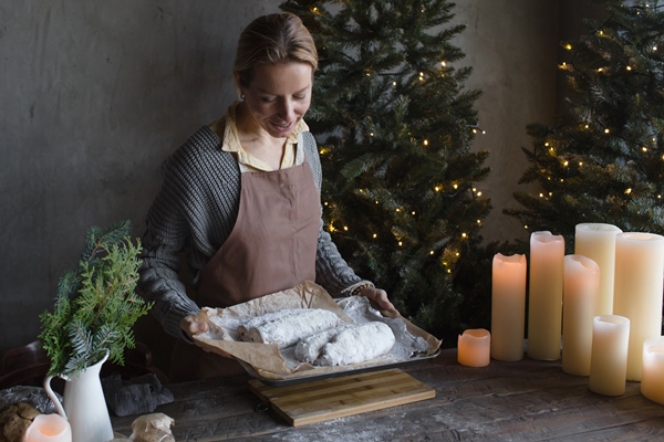 a woman in a kitchen apron is preparing a christmas stollen a woman holds a pie on a wooden tray at christmas - Марципановый штоллен