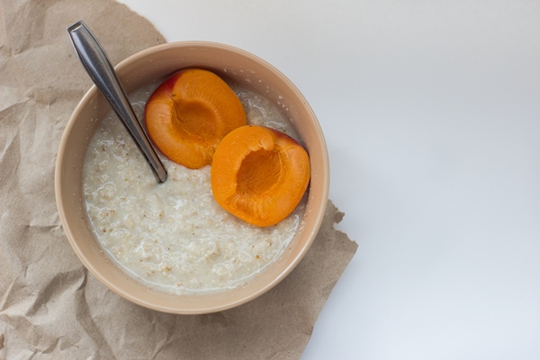 bowl with flakes and apricot on a white surface - Каша жидкая молочная овсяная (школьное питание)