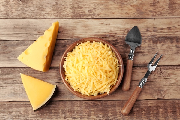bowl with grated cheese on wooden background - Салат с крабовыми палочками, сыром, яйцом и черносливом