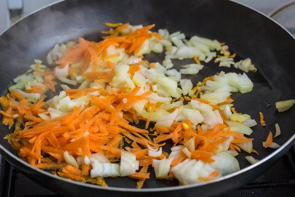 crushed onions and carrots in a frying pan and wooden spatula homemade dishes vegetarianism - Рассольник с рисом (школьное питание)