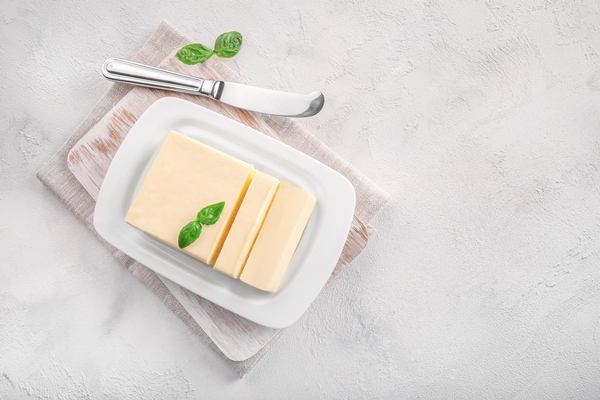 cut block of fresh butter in white ceramic butter dish on white - Салат с крабовыми палочками, сыром, яйцом и черносливом