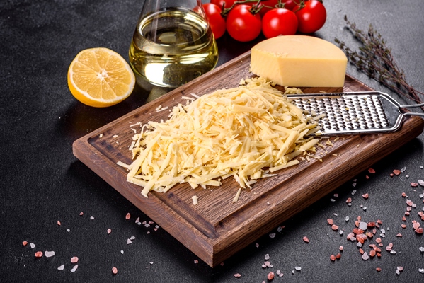 fresh hard cheese grated on a large grater on a wooden cutting board on a dark concrete background 1 - Макароны отварные с сыром (школьное питание)