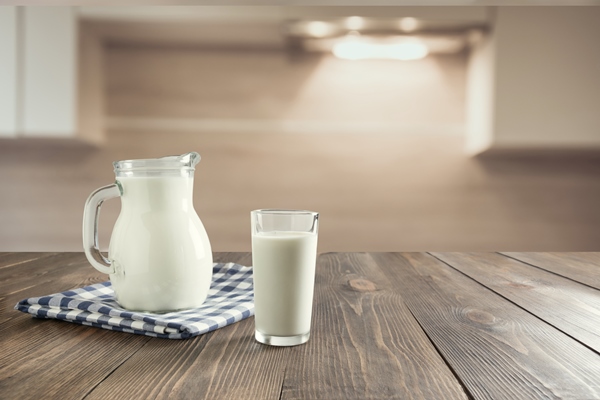 glass of fresh milk and jug on wooden tabletop with blur kitchen as background - Картофель отварной в молоке (школьное питание)