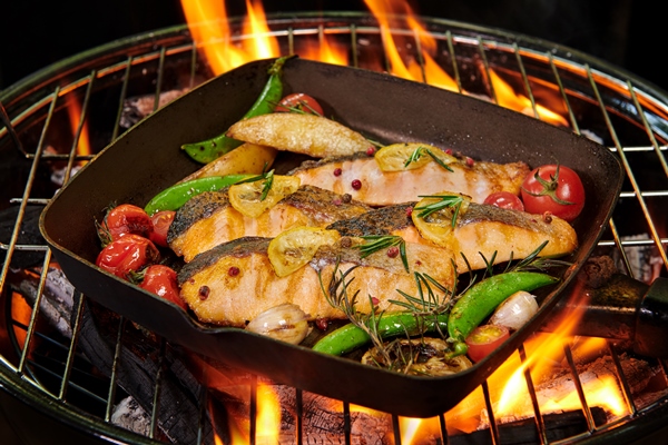 grilled salmon fish with various vegetables on pan on the flaming grill pepper lemon and salt herb decoration - Стейк из лосося