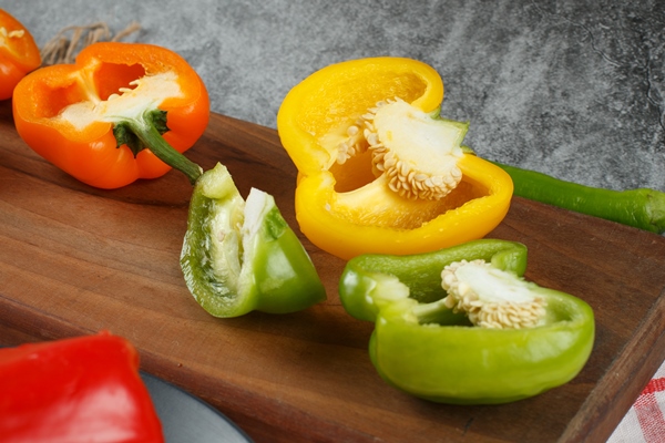 half cut colorful bell peppers on a wooden board - Постный салат с тунцом "Новогодний"