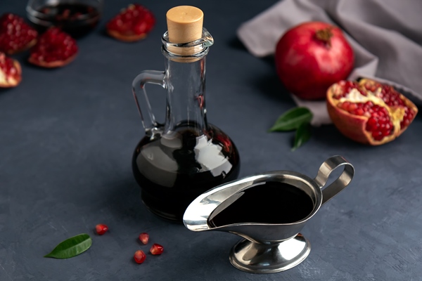 pomegranate sauce in a bottle and gravy boat with grains and pieces of pomegranate on dark - Постный салат из фасоли, граната и грецкого ореха по-грузински