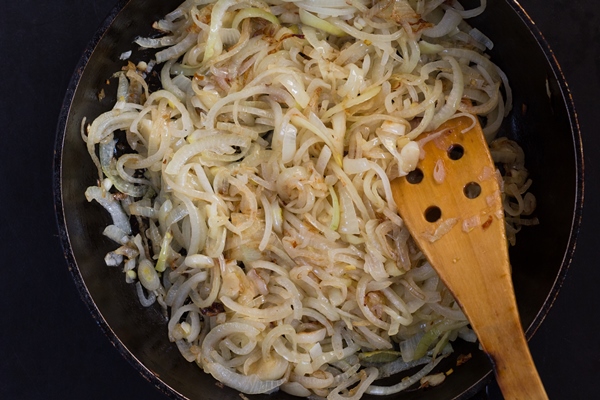 top view of frying or caramelizing cut onion on pan on the black background 1 - Постный салат из фасоли, граната и грецкого ореха по-грузински
