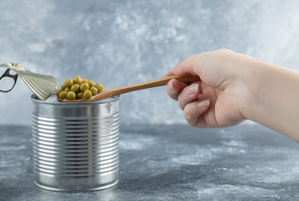 woman taking green peas from tin with spoon over grey table - Омлет с зелёным горошком (школьное питание)