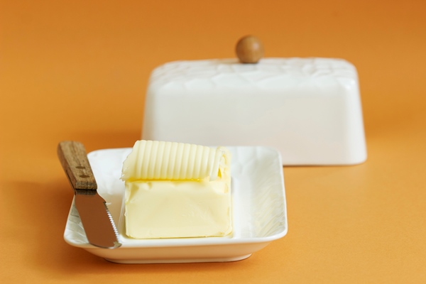 a piece of butter in butter dish and a knife on a colored background selective focus - Омлет с сыром (школьное питание)