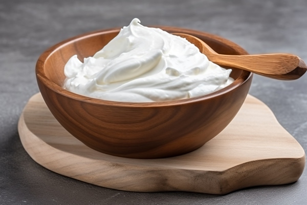 a wooden bowl filled with whipped cream on a wooden board - Сырники (школьное питание)
