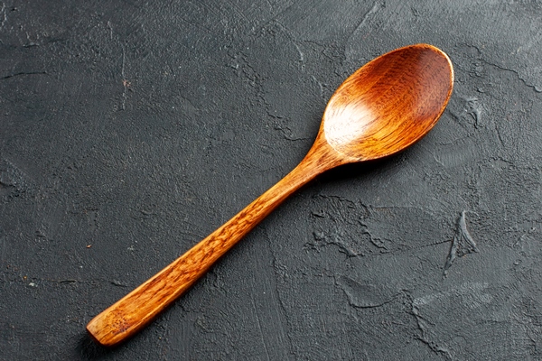 bottom view wooden spoon on dark surface with free space - Секреты приготовления киселей на крахмале