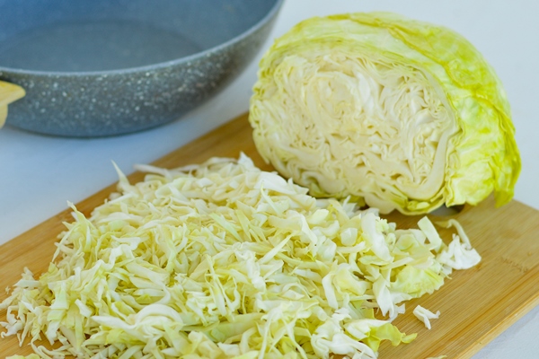 cabbage cut into strips is lying on a wooden kitchen board ready for stewing - Ленивые голубцы (школьное питание)